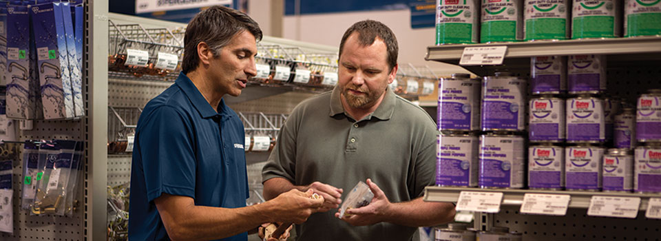 A Ferguson associate discusses a pipe he’s holding with a contractor in a plumbing counter aisle.