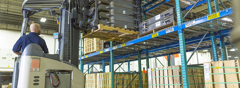A Ferguson associate operates a forklift and lifts a pallet of HVAC supplies from a warehouse shelf.