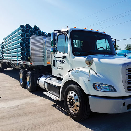 A Ferguson 18-wheeler truck carrying stacks of pipe is parked on concrete.