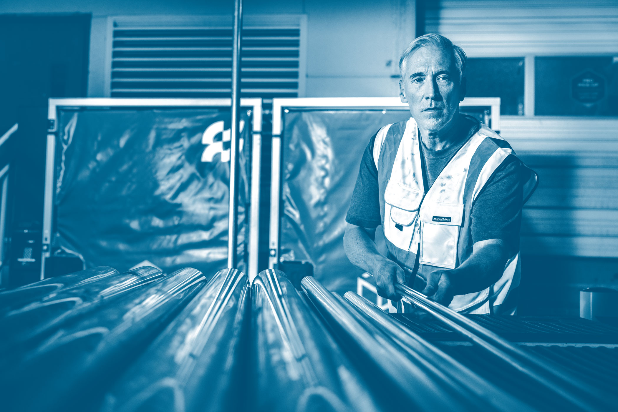 A man wearing a reflective vest places pipe in the flatbed of a truck.